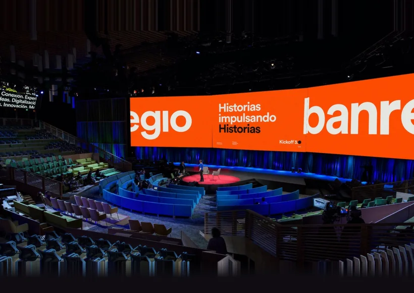 Auditorio del kickoff de Banregio: la pantalla curva envuelve el escenario con la gráfica naranja de la marca